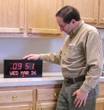 Photo of a man standing beside the Big Digital LED Calendar Clock that is set on a counter top.