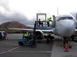 Photo of Bill sitting in an aisle chair, inside a clear enclosed box, being lifted by a forklift to a plane door.