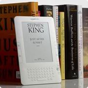 photo of a Kindle leaning against a row of hard-backed books. The display of a Stephen King novel is on the Kindle.